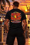 A man stands on a dock at sunset wearing a black T-shirt with a large 'Kage Kombat San Pedro' graphic on the back, with a tropical harbor and port cranes in the background.